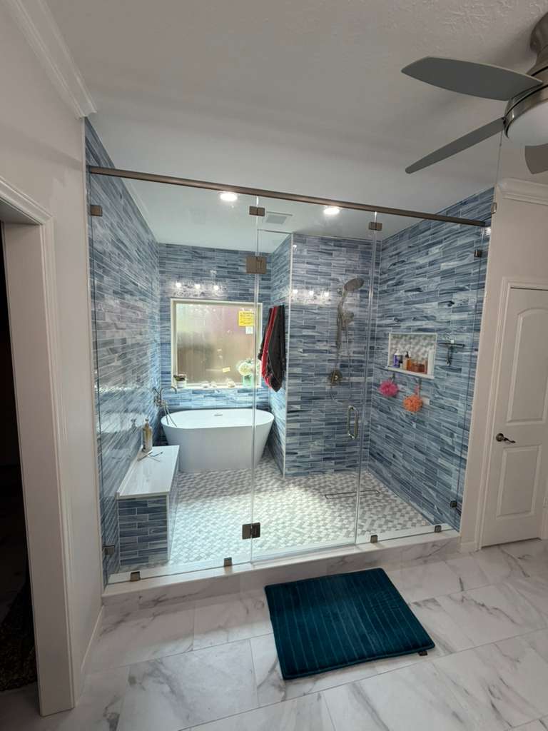 Large frameless steam shower enclosure with blue mosaic tile and freestanding tub
