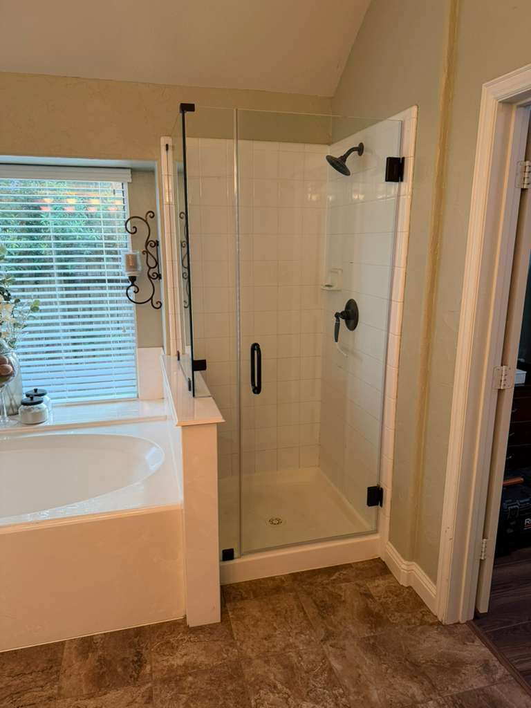 Frameless shower door with oil-rubbed bronze hardware next to garden tub